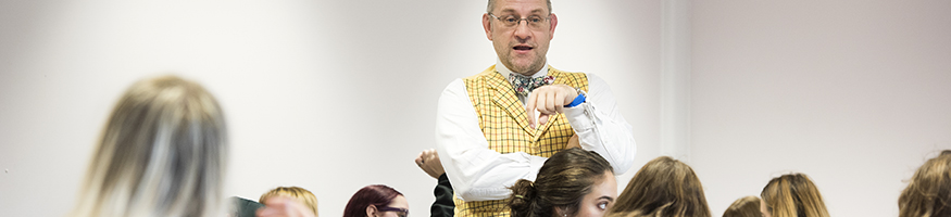 Tutor in yellow waistcoat engaged in discussion with students in classroom